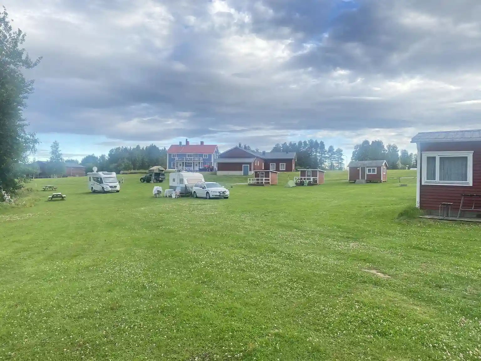 En vidsträckt grön gräsmatta sträcker sig under en molnig himmel vid Åmsele camping. Området är öppet och inbjudande, omgivet av natur.