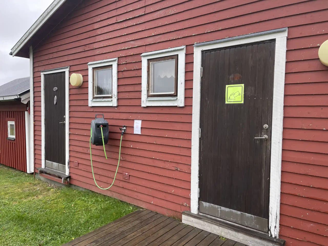 En stuga vid Åmsele camping med träfasad och en enkel dörr, omgiven av lummig grönska.