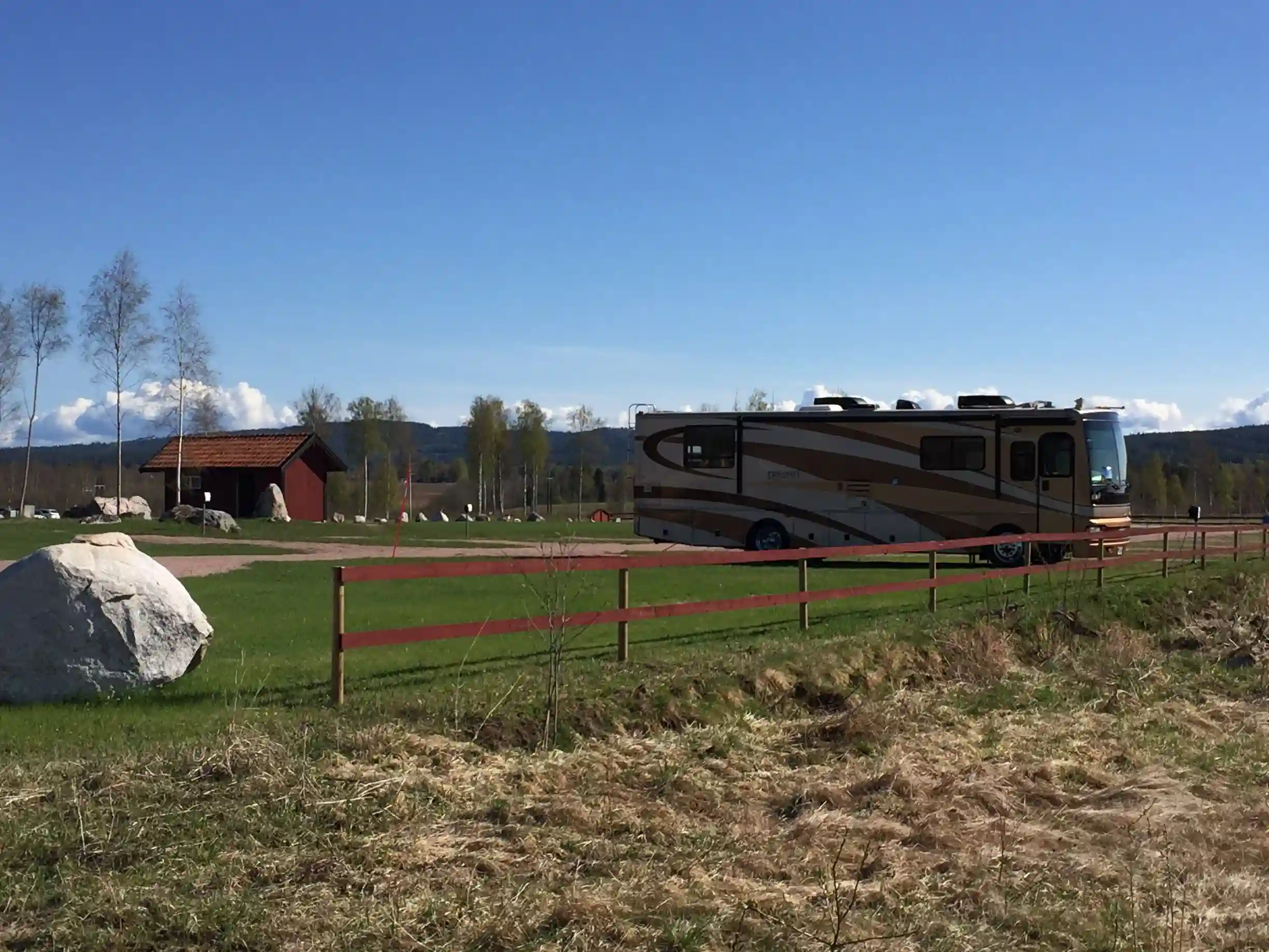 En husbil står parkerad på en grön äng under en molnig himmel, omgiven av vidsträckta gräsmarker i ett landsbygdsområde i Dalarna.