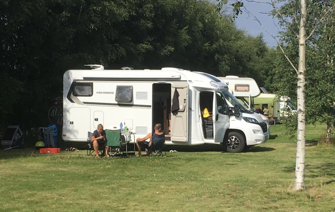 En husvagn står parkerad på en grön campingplats vid Bläsinge Gård, omgiven av natur och rekreationsområde.