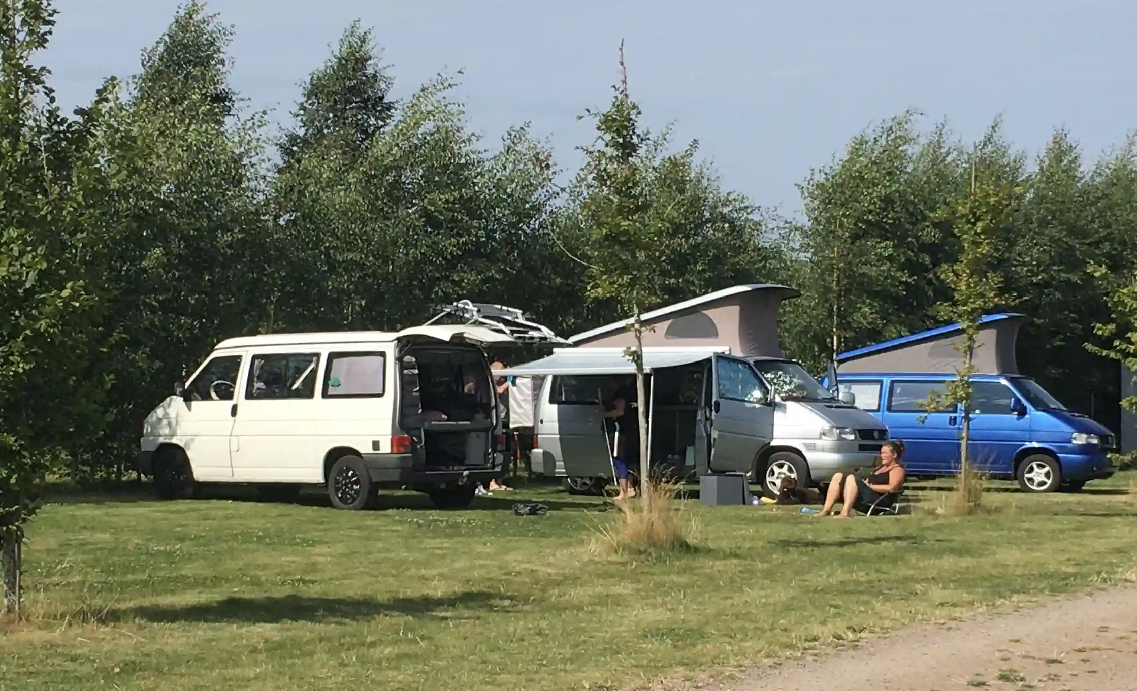 En vit skåpbil parkerad vid Bläsinge Gård, omgiven av grönska och en grusväg. Bilen, med tydliga däck och karossdetaljer, står i fokus framför gården.