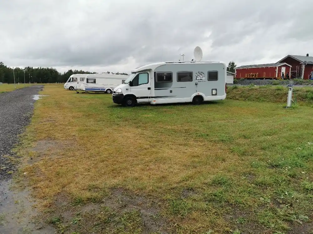 En vit husbil som står parkerad på en grusplan, omgiven av gröna träd under en klar himmel vid besöksmålet Cape East.