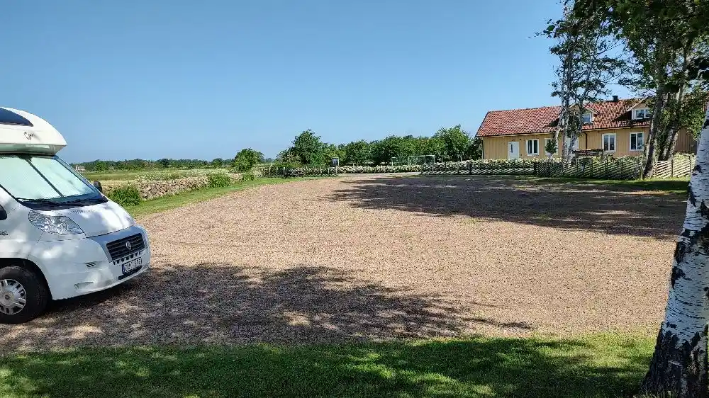 Bild av Björkängs vandrarhem med en gräsmatta och infart. En husbil och mindre bil står parkerade på uppfarten. Området är landskapsplanerat och omges av trädgårdsmiljöer.