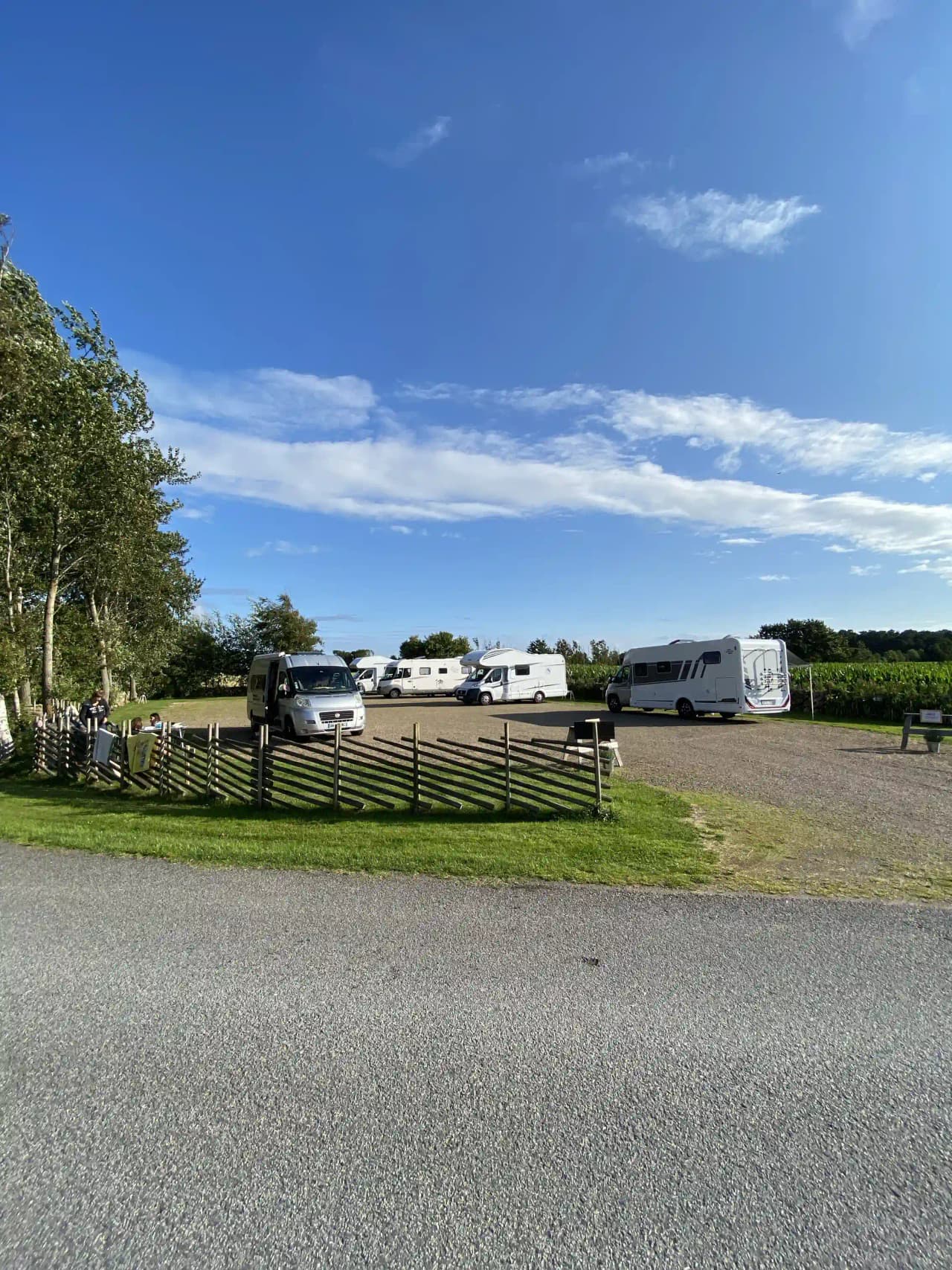 En husvagn står parkerad på en asfalterad uppfart vid Björkängs vandrarhem, omgiven av gröna gräsmattor och en himmel med vita moln.