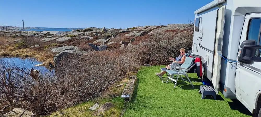 En campingplats med flera husvagnar och husbilar uppställda på gräsytor hos Sotenäs Camping, omgiven av grönska under en klar himmel.