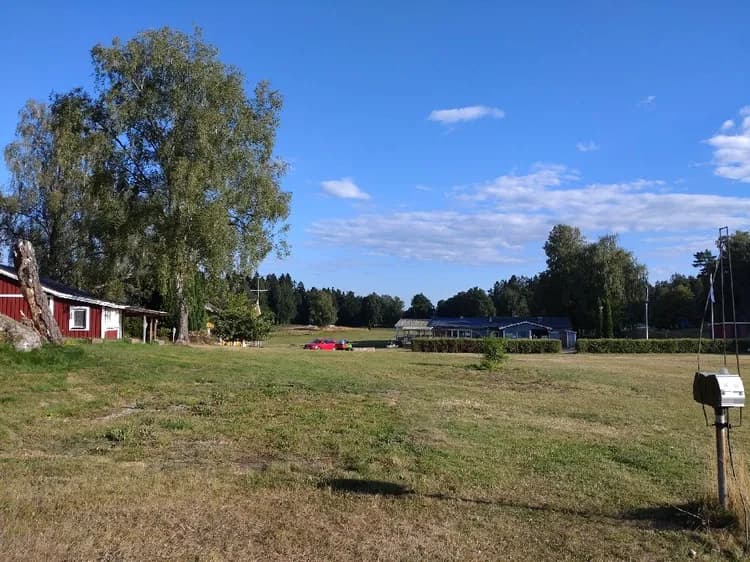 En grönskande äng vid Farstanäs camping & havsbad, omgiven av träd och molnig himmel.