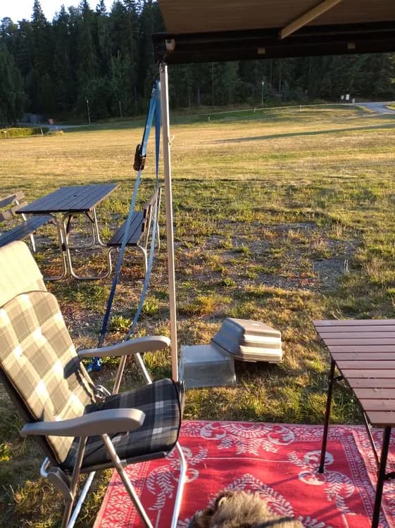 En campingplats med trädgårdsmöbler inklusive fällbara stolar och ett bord, omgiven av grönskande gräsmatta. Skugga från träd i bakgrunden ger en inbjudande atmosfär vid Farstanäs Camping & Havsbad.