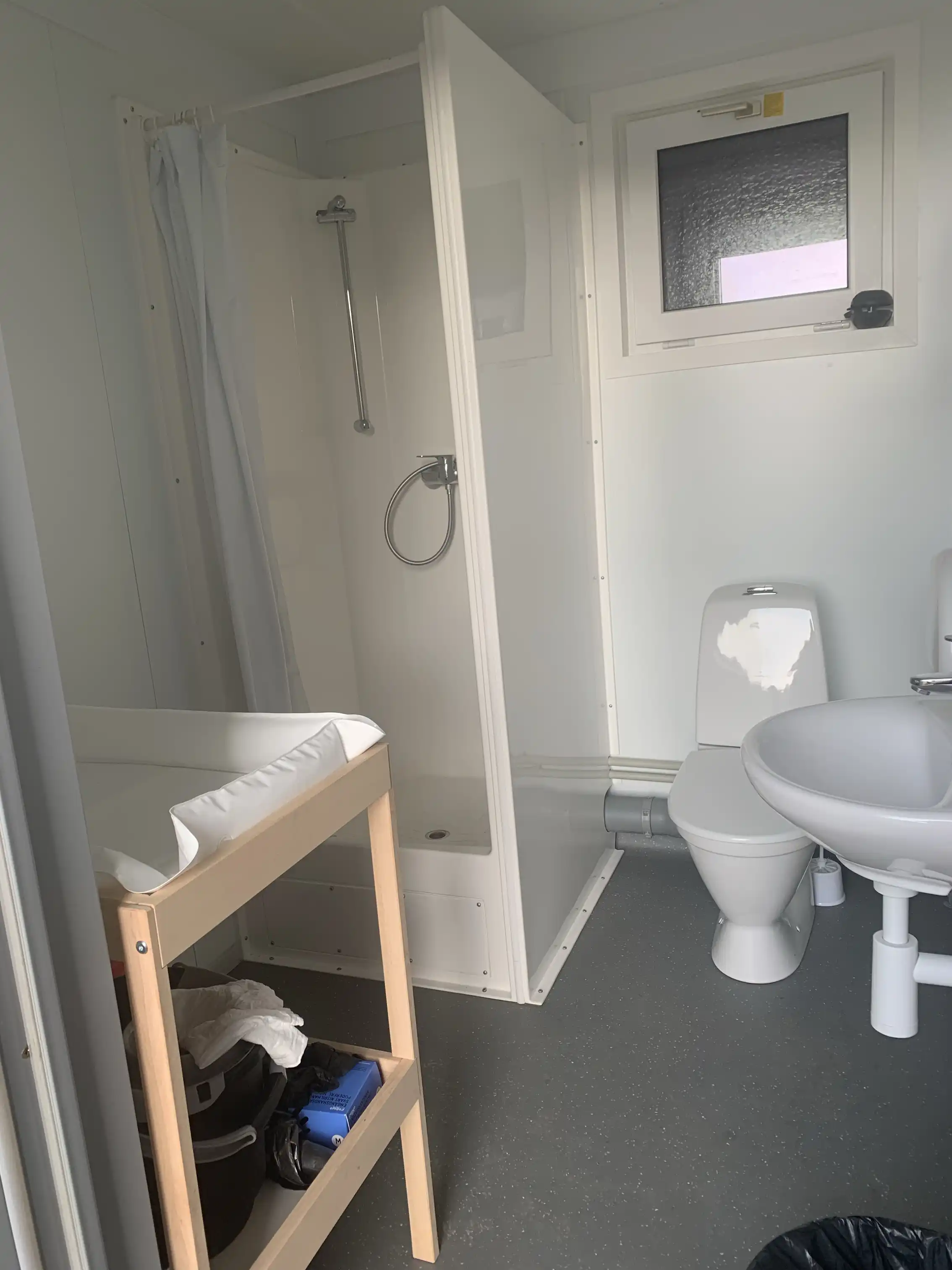 Bild av ett rum på Gunnagård med träinredning och golv. Rummet innehåller VVS-installationer, inklusive ett tvättställ, samt en dörröppning och ett tak som matchar inredningens trätema.