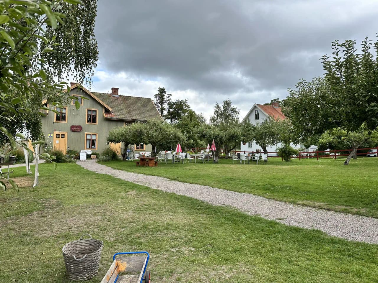 En vacker vy av ett glasbruk med historiska byggnader omgivna av gröna gräsmattor och lummiga trädgårdar, beläget i en lantlig miljö.