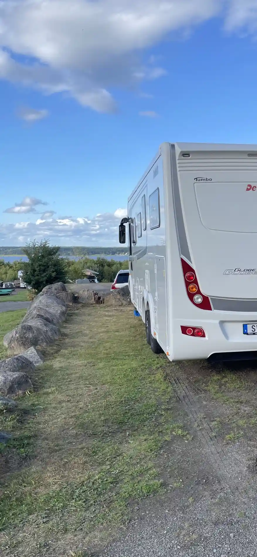 En husbil står parkerad på Tostarps camping, läger- och kursgård. Bilden visar sidan av fordonet med speglar och dörrar synliga.