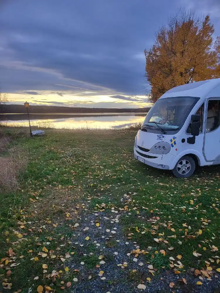 En grusparkering vid Trångsvikens bygdegård med flera parkerade husbilar och minibussar.