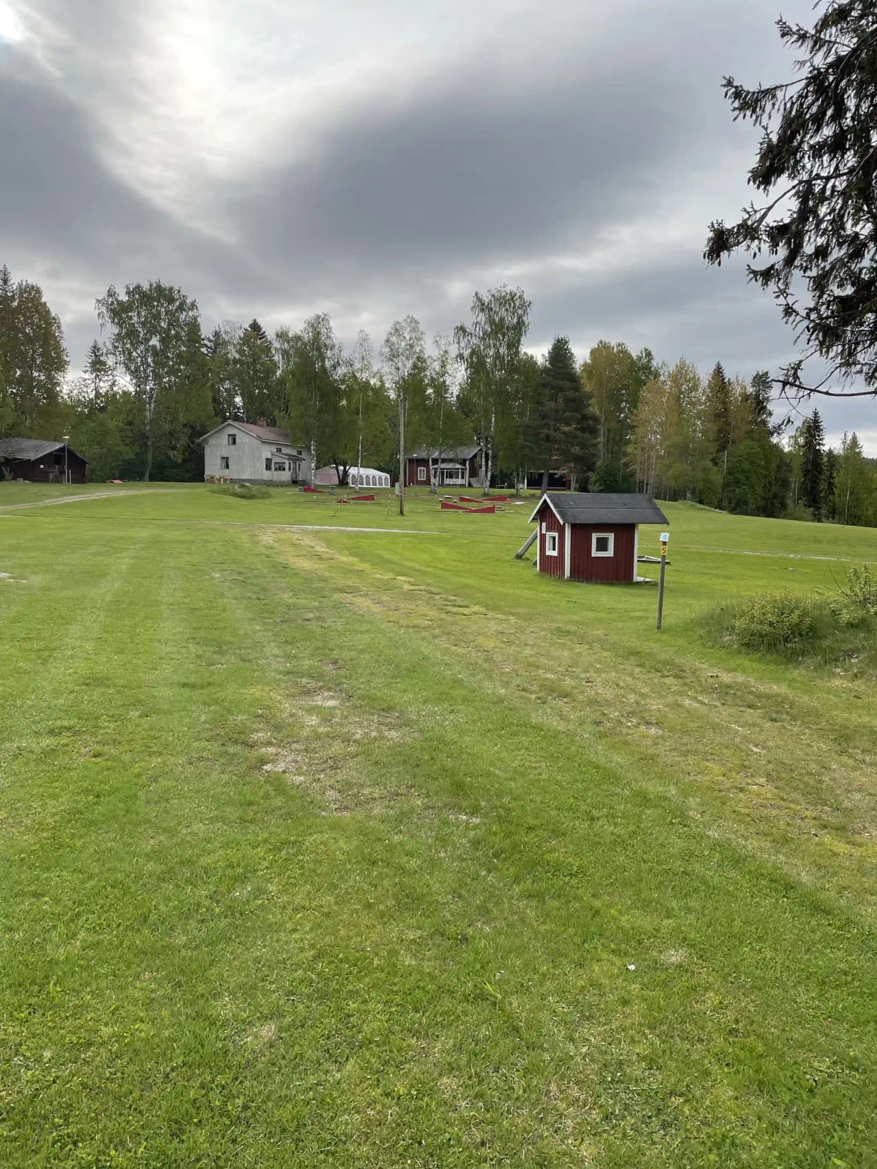 Bild av Valasjöns camping: en grönskande campingplats med frodig gräsmatta och flera träd. I bakgrunden syns ett stugliknande hus som ger en inbjudande och naturnära atmosfär.