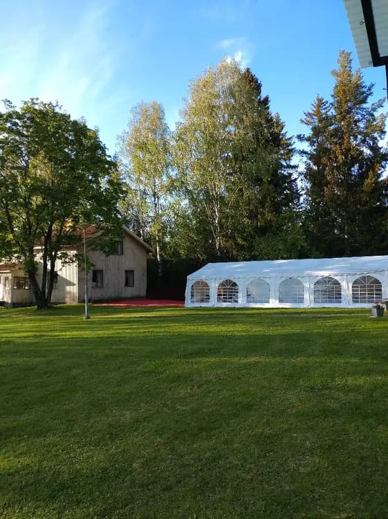 En grönskande campingplats vid Valasjön med tält uppställda på en välskött gräsmatta omgiven av höga barrträd som ger skugga.