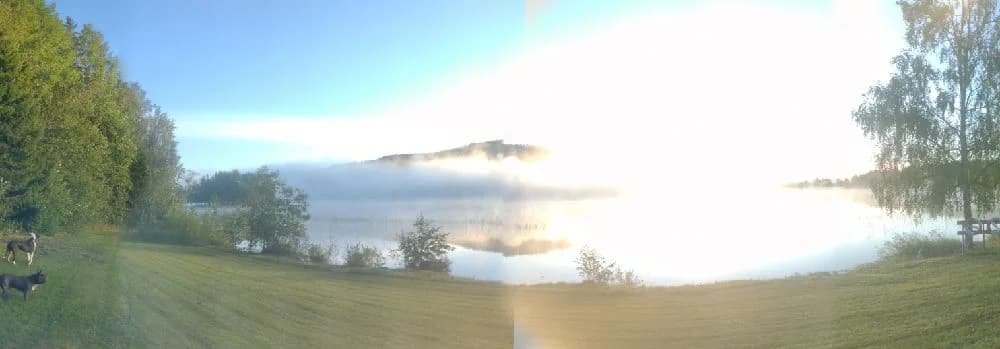 En vacker morgon vid Valasjöns camping med soluppgång som skapar linsöverstrålning och spegelblank sjö som reflekterar landskapet.