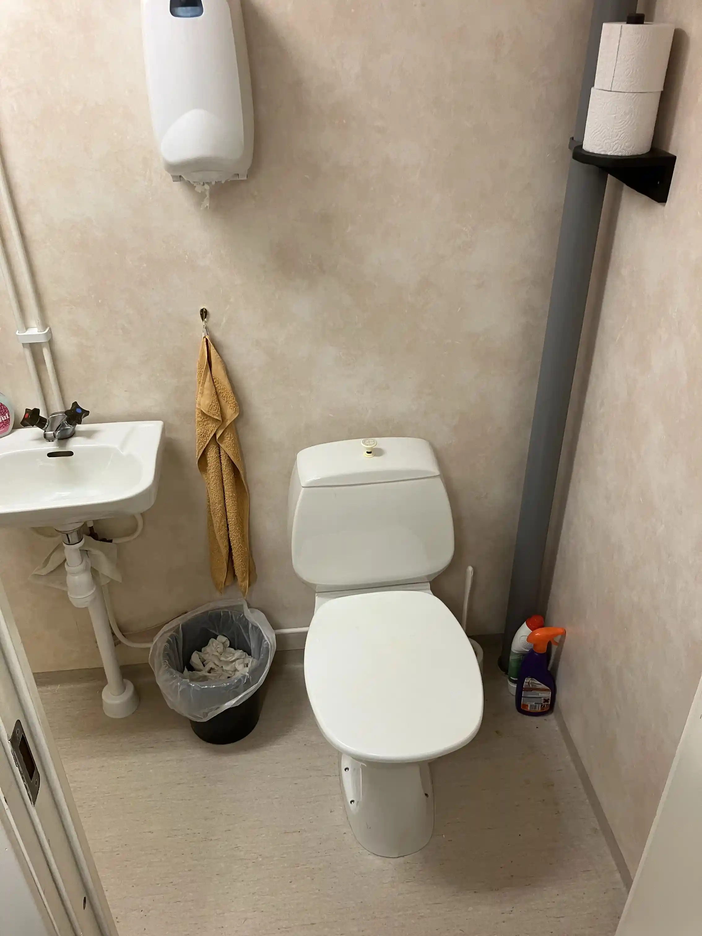 En vit toalettstol i ett badrum med mörka kakelgolv och ljusa väggar. Inredningen är enkel och funktionell.