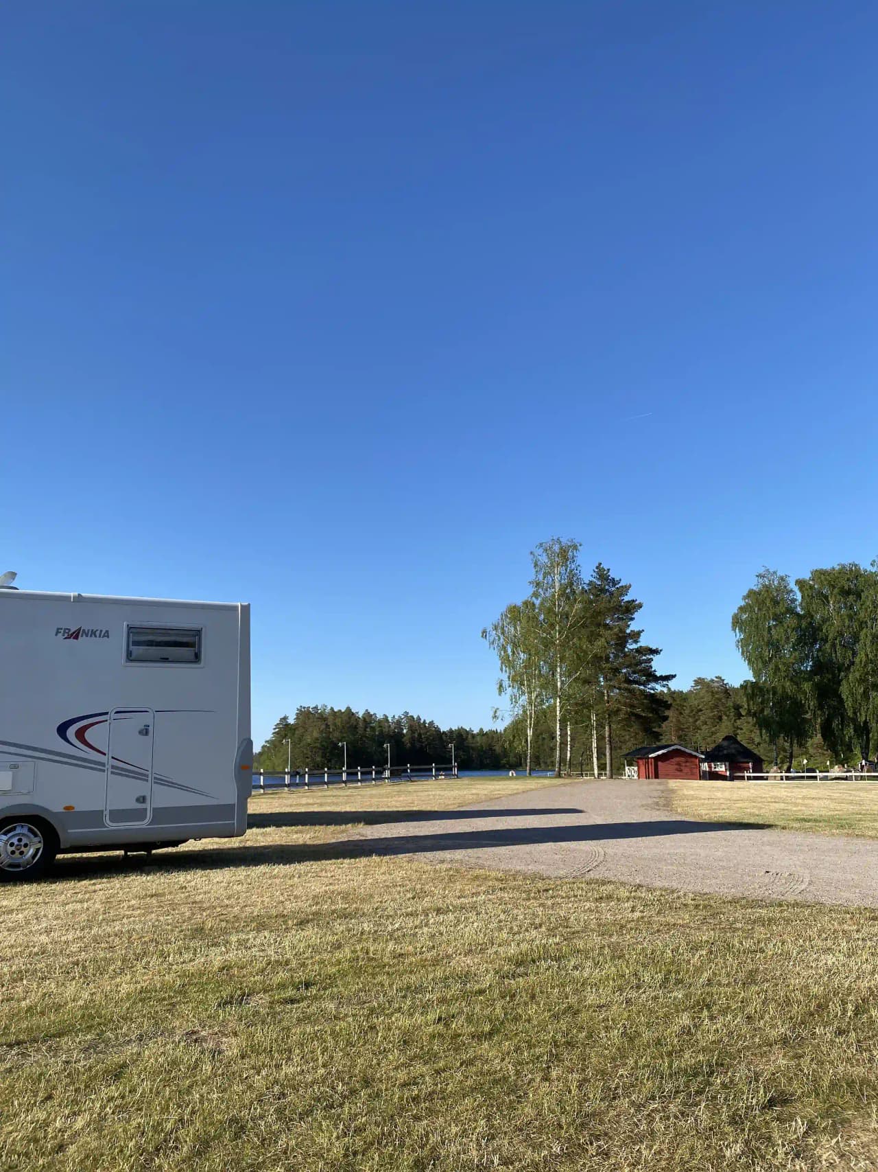 En rad med husvagnar och mobilhem parkerade nära varandra på en campingplats i ett skuggigt område.