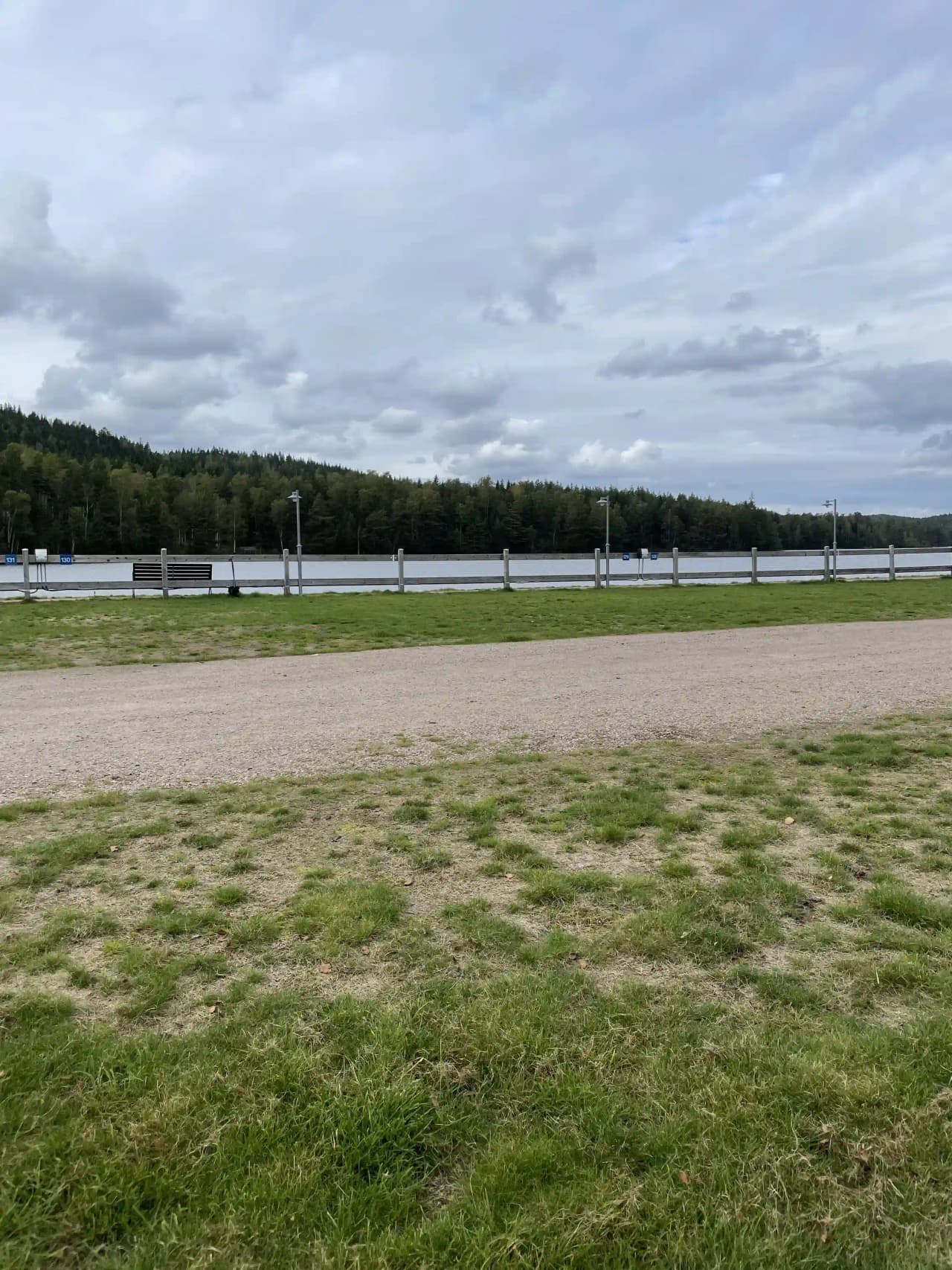 En öppen gräsyta med staket i förgrunden, omgiven av molntäckt himmel, belägen på Överlida Camping.