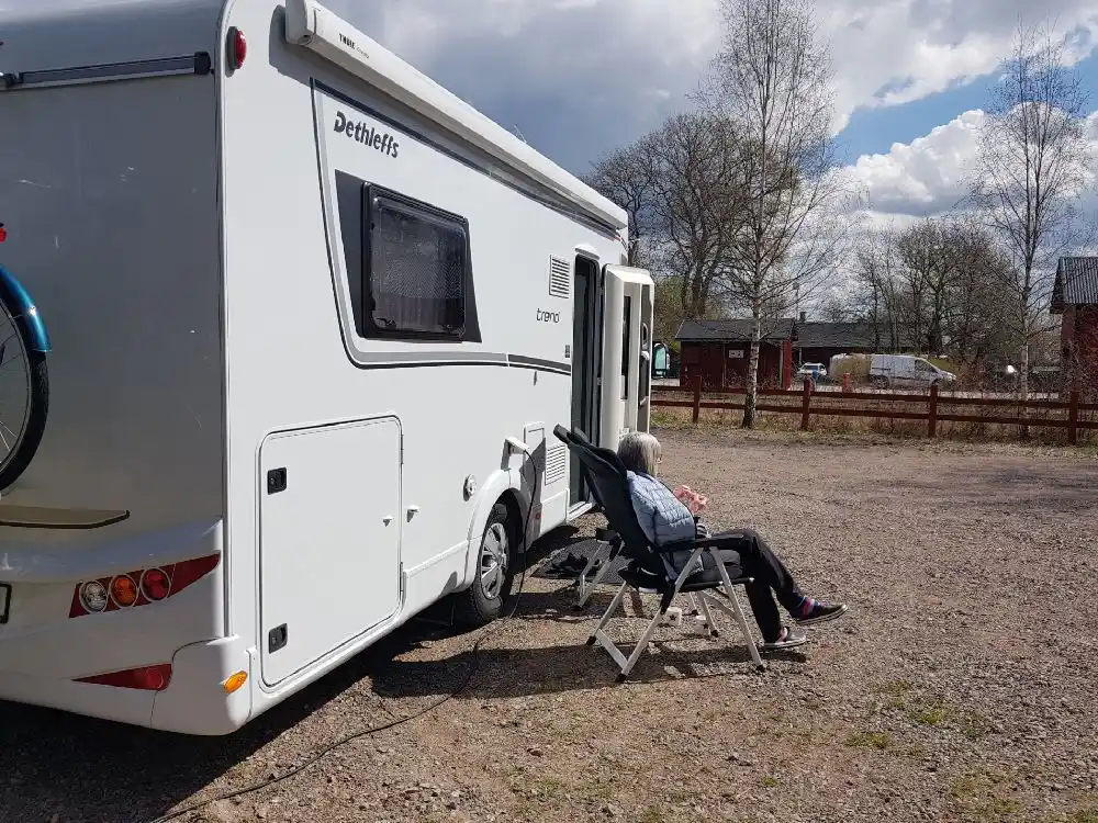 En husvagn står parkerad vid Vimmerby Camping - Nossenbaden, omgiven av grönskande natur och med några campare som njuter av utomhusmiljön.