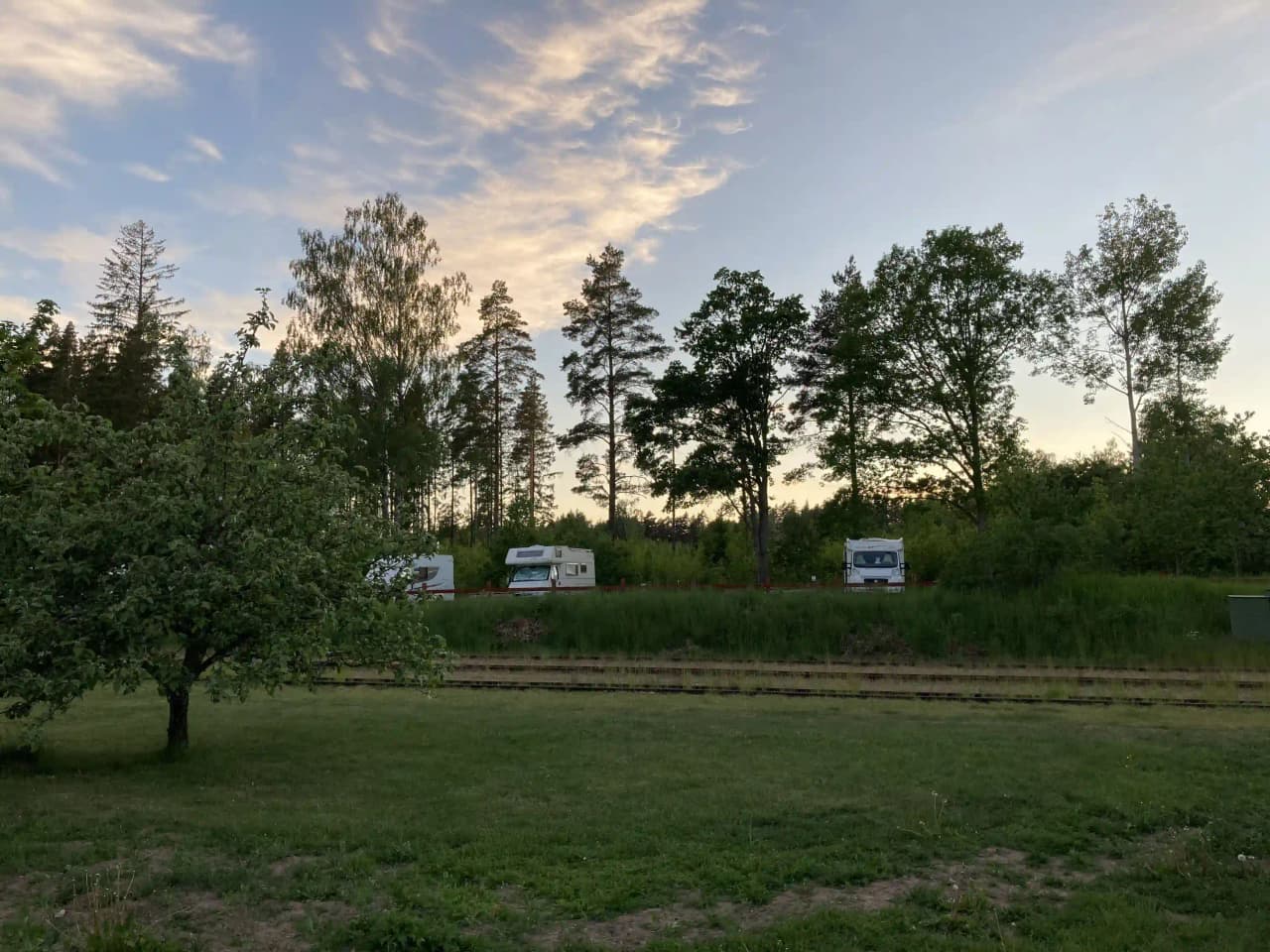 Bild av en grön campingplats i Vimmerby vid Nossenbaden, omgiven av träd och buskar, med en husbil parkerad på ett öppet gräsområde.