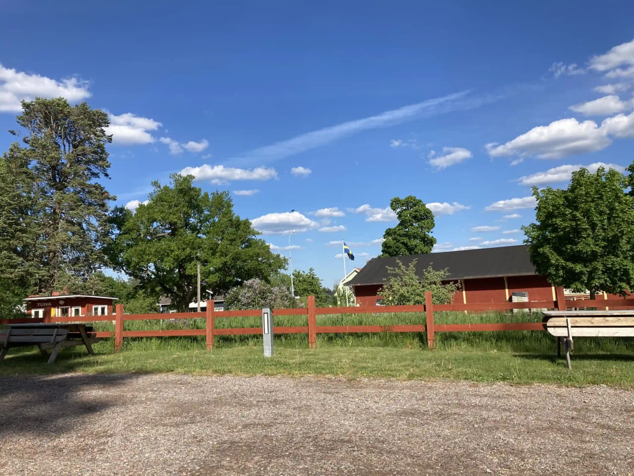 Bild av en grön och öppen campingplats i Vimmerby med välklippt gräsmatta. I bakgrunden syns låga träd och ett staket. Det finns ett fåtal skuggiga områden över platsen.