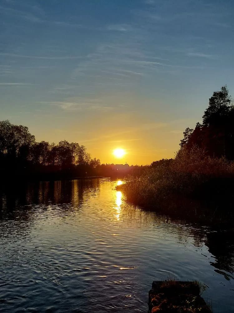 En stilla sjö under solnedgången med horisonten i fjärran, omgiven av naturlandskap och himmel.
