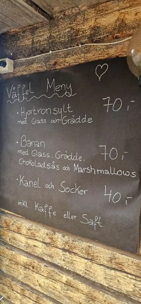 En träplanka med handskriven meny i krita, uppsatt i Hamra Stugby. Bakgrunden består av rustikt brunt trä, vilket ger en varm och inbjudande känsla.