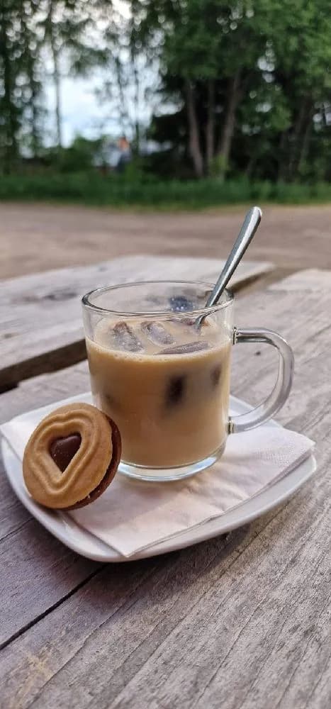 En inbjudande bild på en kaffekopp fylld med skummig café au lait, omgiven av porslin och koppar på ett bord, i en trivsam miljö vid Hamra Stugby.