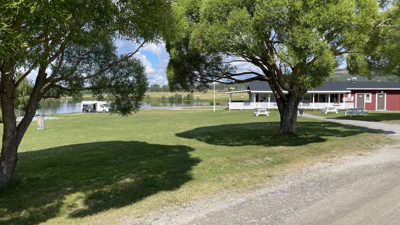 Bild av Långsele camping som visar en idyllisk stuga omgiven av grönt gräs och träd, vilket skapar en lugn och naturskön miljö.