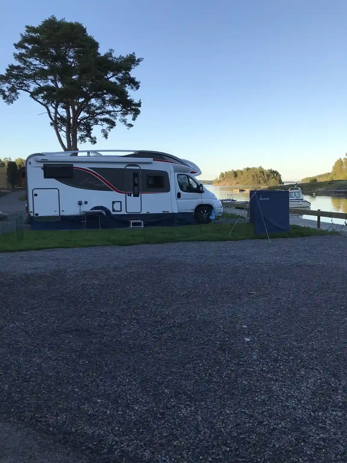 En campingbil är parkerad vid Eriksviks hamn, omgiven av andra fordon och med speglingar i sidobackspeglarna.