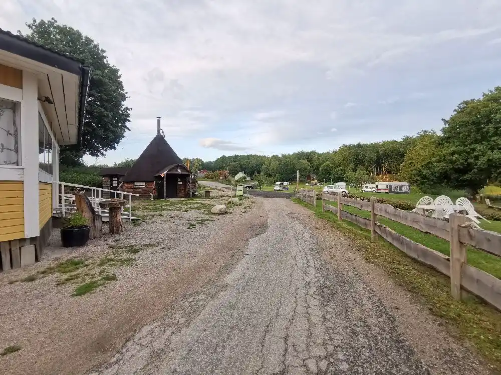 En lantlig vy vid Ljuvadal camping & ställplats med stugor omgivna av gröna ängar, en grusväg och molniga himlar i bakgrunden.