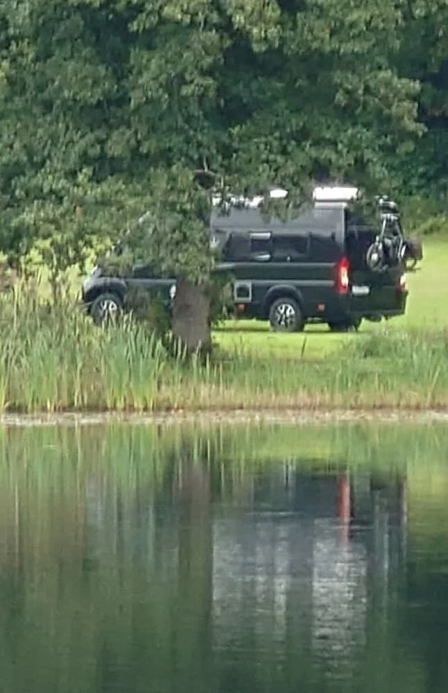 En campingplats med flera husbilar och husvagnar som är parkerade på grönt våtmarksområde. Träden omger platsen som ger ett lugnt och naturnära intryck.