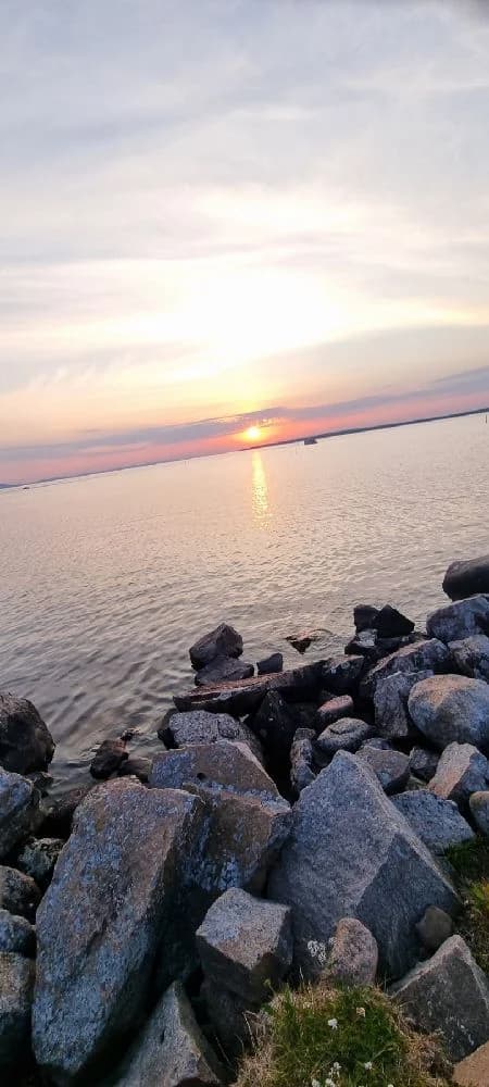 En solnedgång vid Tällbergs camping med en himmel fylld av mjuka moln och ett efterglödande sken. I förgrunden syns klippor vid vattenbrynet och havets lugna yta som reflekterar kvällens ljusspel.