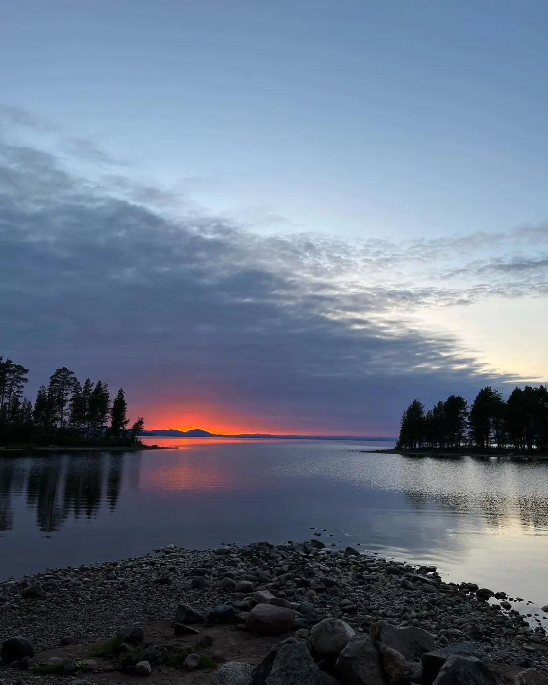En naturskön vy över ett lugnt vatten i skymningen med mjuka moln och blå himmel i bakgrunden, fångat vid Tällbergs Camping.