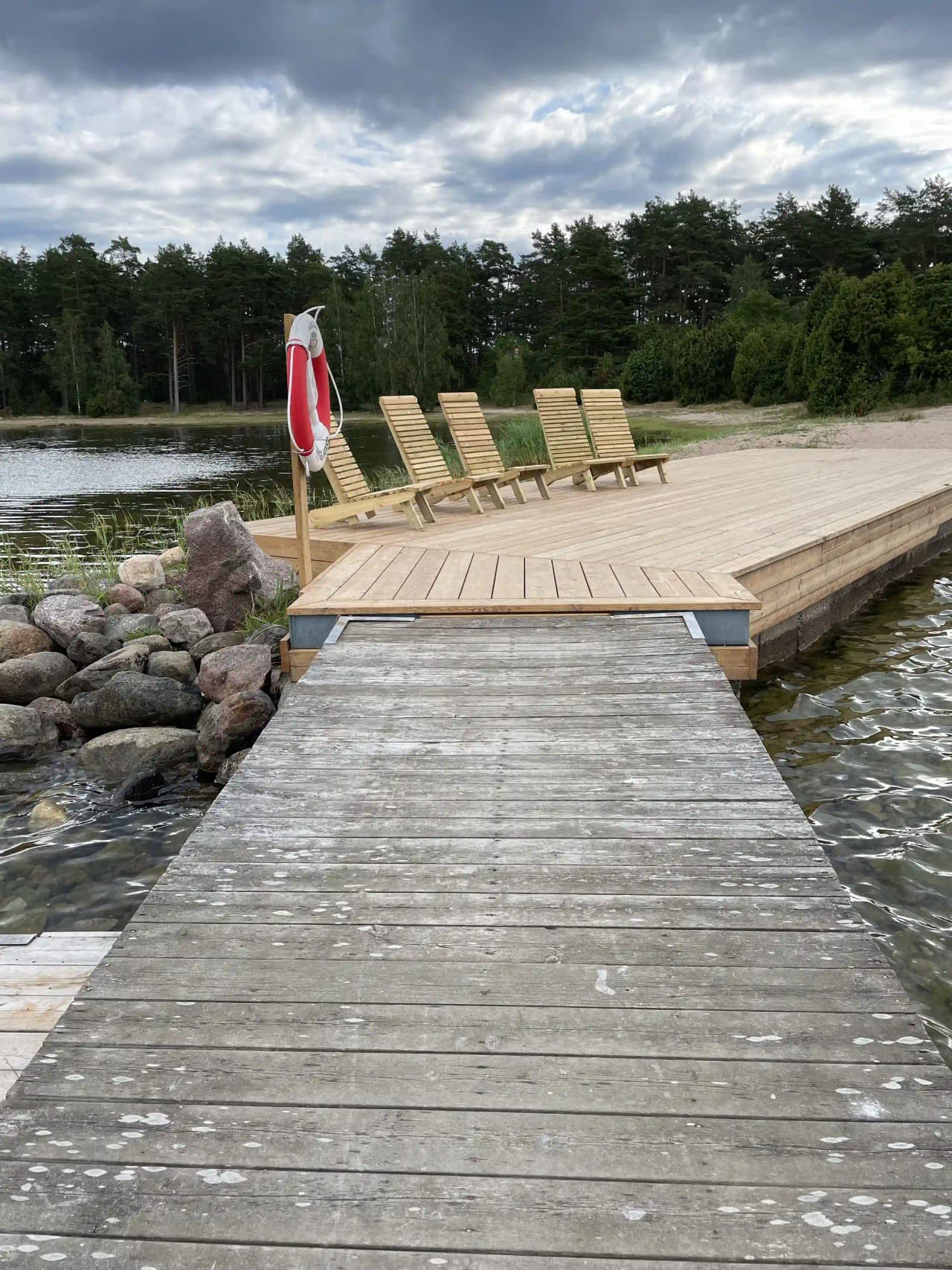 En träbrygga leder ut över en stilla sjö, omgiven av frodig grönska vid Kaffetorpets camping.
