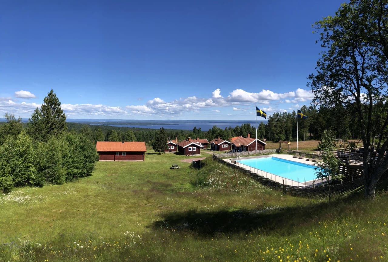 En rustik stuga med utomhusmöbler, omgiven av grönskande natur vid Åsengården, perfekt för avkoppling och vistelser i ekologisk miljö.