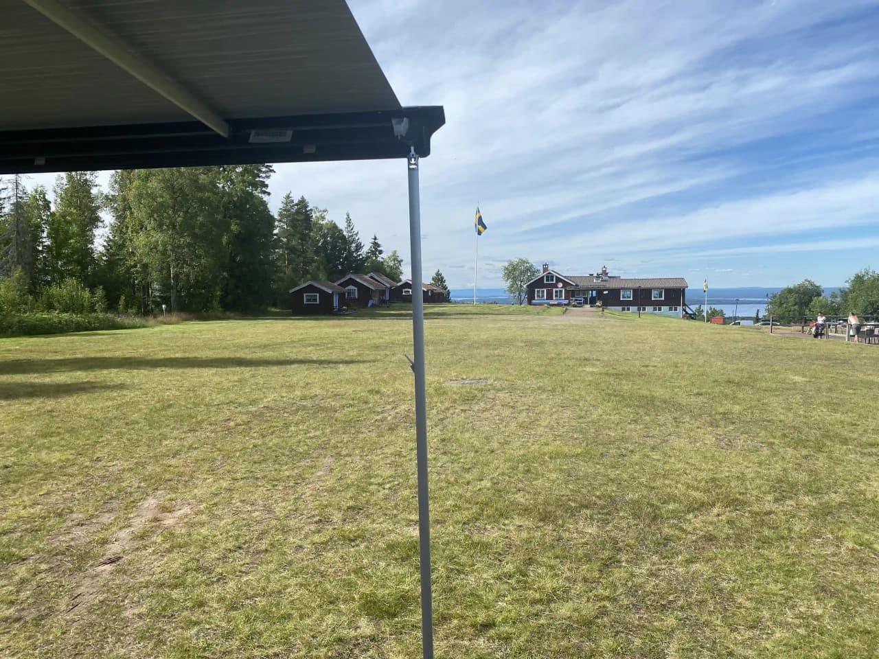 Bild av Åsengården: en lummig gräsbevuxen mark med skuggiga områden, omgiven av ett staket och utomhusstruktur.