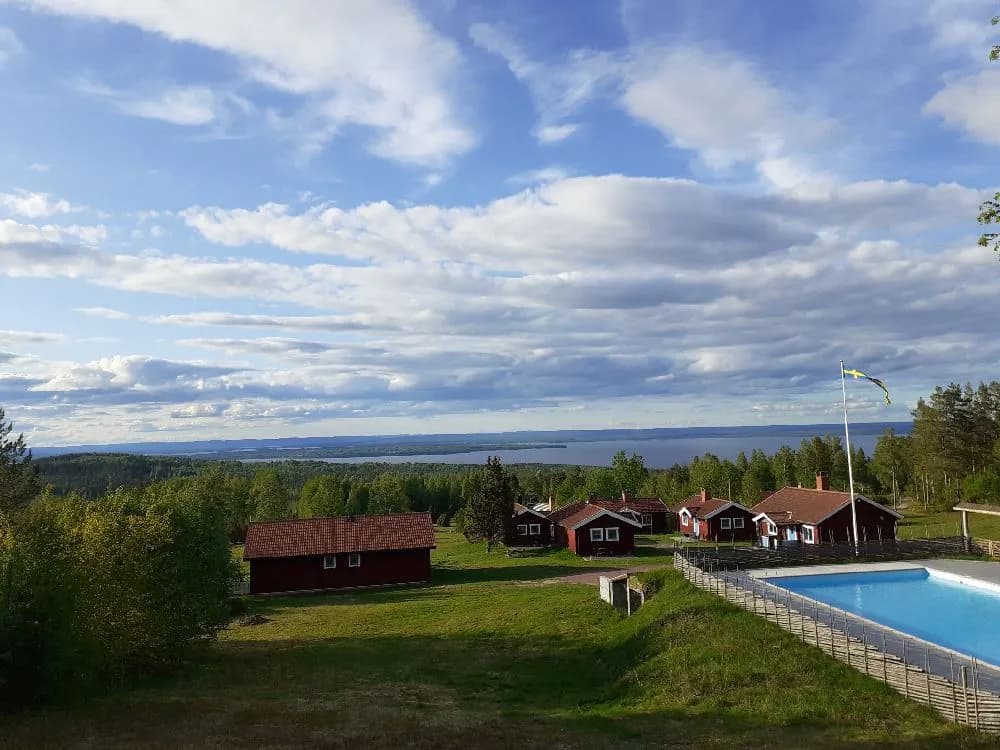 Bild av Åsengården: En lantlig stuga omgiven av en grön gräsmatta och trädgårdsbyggnader, med en bakgård som ger en känsla av ett ekologiskt hotell eller bondgård.