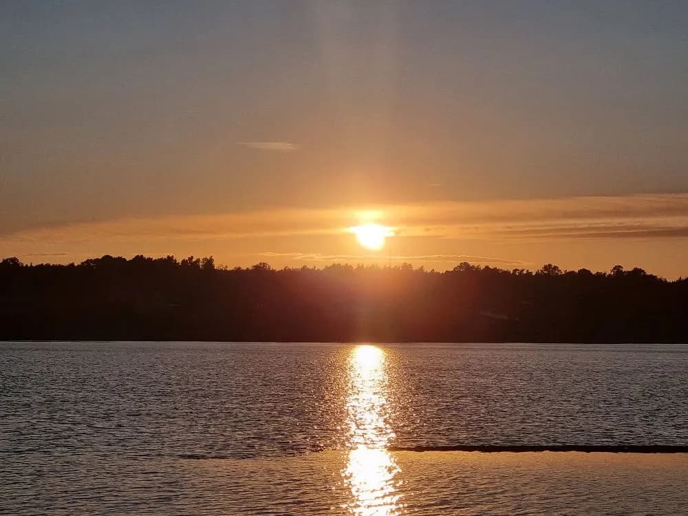 En vacker solnedgång över ett vattenlandskap i målsånna camping park, med en klar himmel där solen möter horisonten och vattnet speglar de varma färgerna.