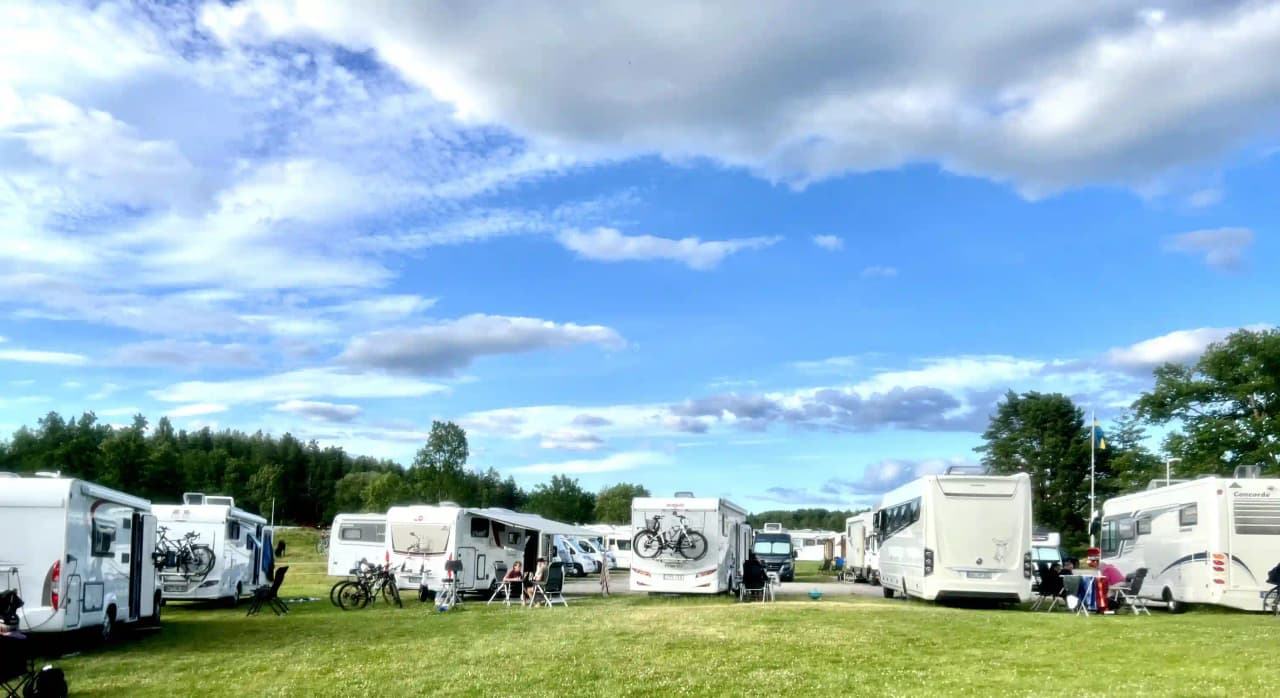 Bild av Upperuds Gästhamn med husbilar och husvagnar parkerade vid en campingplats. Det är molnigt väder och platsen omges av gröna träd och natur.