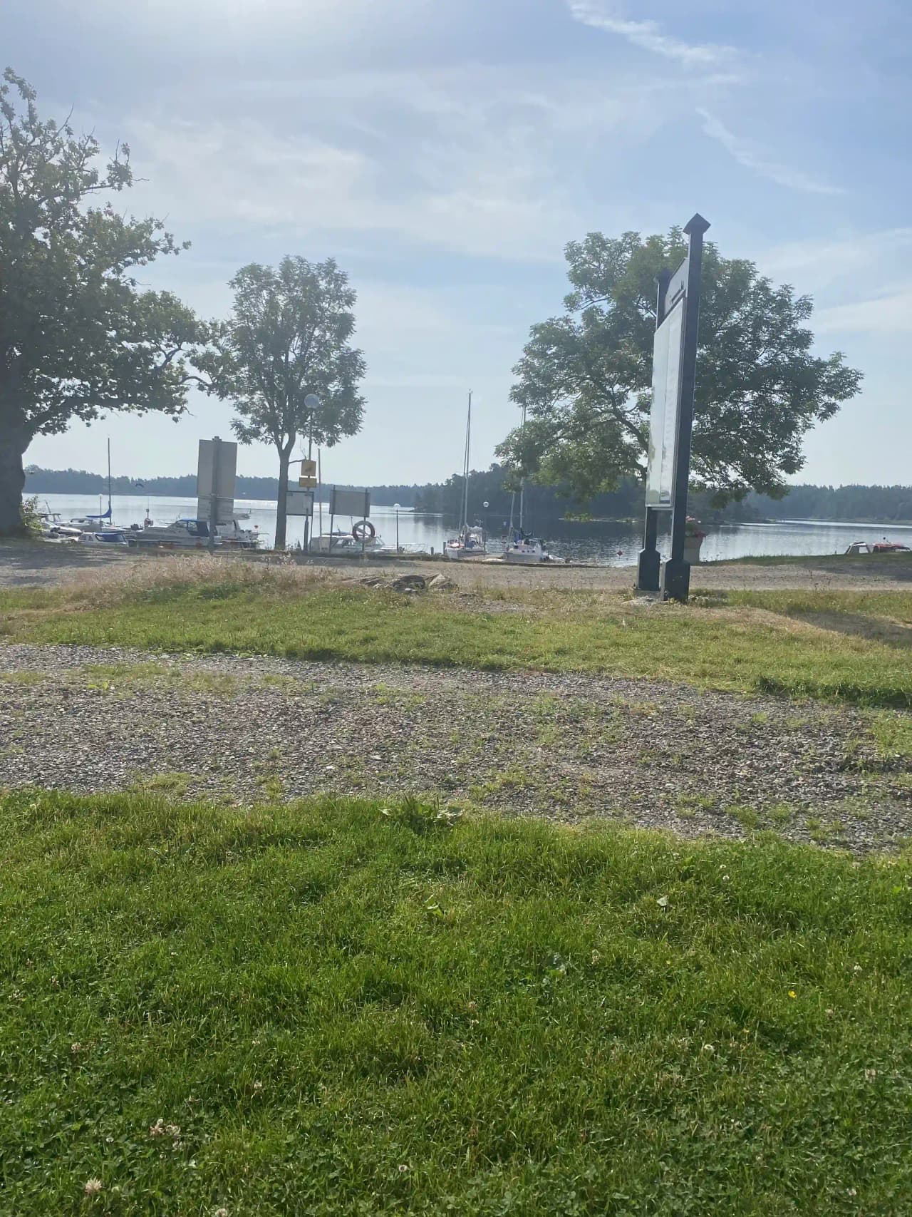 En bild av Upperuds Gästhamn med molnig himmel ovanför. I förgrunden syns stranden som kantar hamnen, medan frodig grönska från parken omger området.