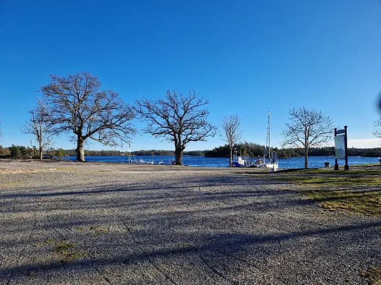 "Blå himmel och moln över Upperuds Gästhamn en solig dag, med naturens grönska längs strandkanten."