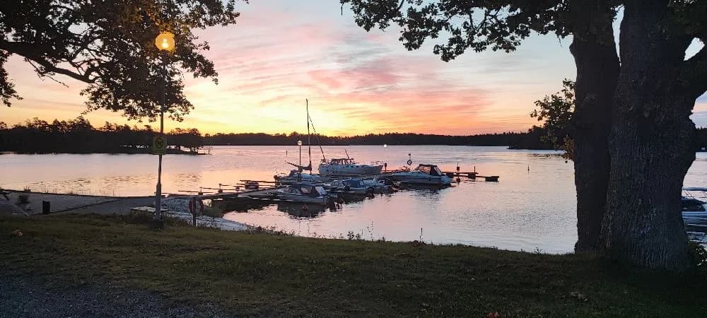 En stilla kvällsbild vid Upperuds Gästhamn med en båt som flyter på det lugna vattnet, omgiven av skymningsljus och en färgglad solnedgång som speglas i himlen och vattnet.