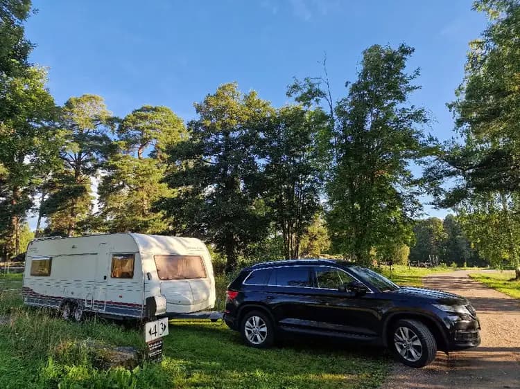 En parkeringsplats vid Mackmyra Bruk och Golf med flera parkerade bilar, inklusive en SUV och en familjebil, i en naturnära miljö.
