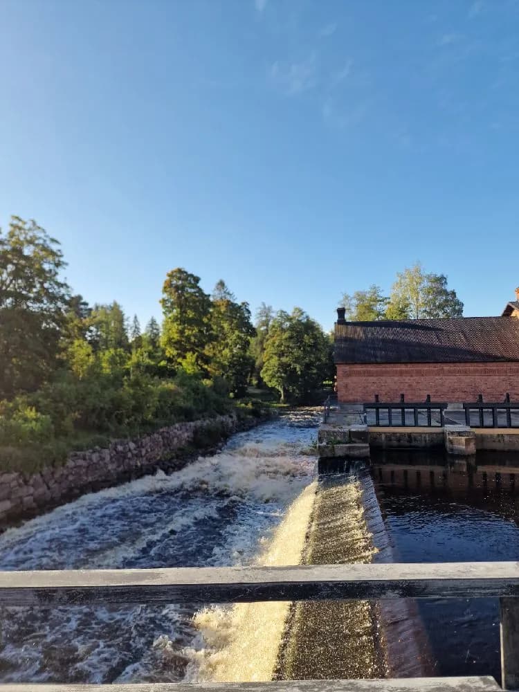 En lugn vattenväg med reflektioner av omgivande landskap, troligen en flod eller kanal vid Mackmyra Bruk och Golf.