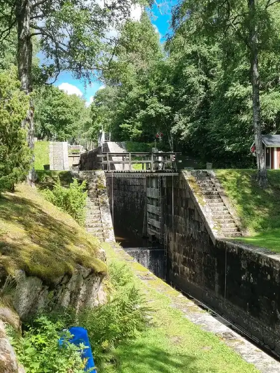 Vy över en pittoresk kanal vid Badsta Camping, med en liten bro som sträcker sig över vattnet. Vattendraget är omringat av grönska, vilket skapar en inbjudande och lugn atmosfär för besökarna.