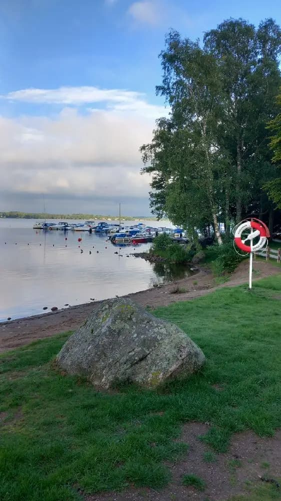 En solig sommardag på Evedals camping vid kusten, med flera båtar förtöjda vid en marina. En motorbåt syns i förgrunden med sin mast rest mot den blå himlen.