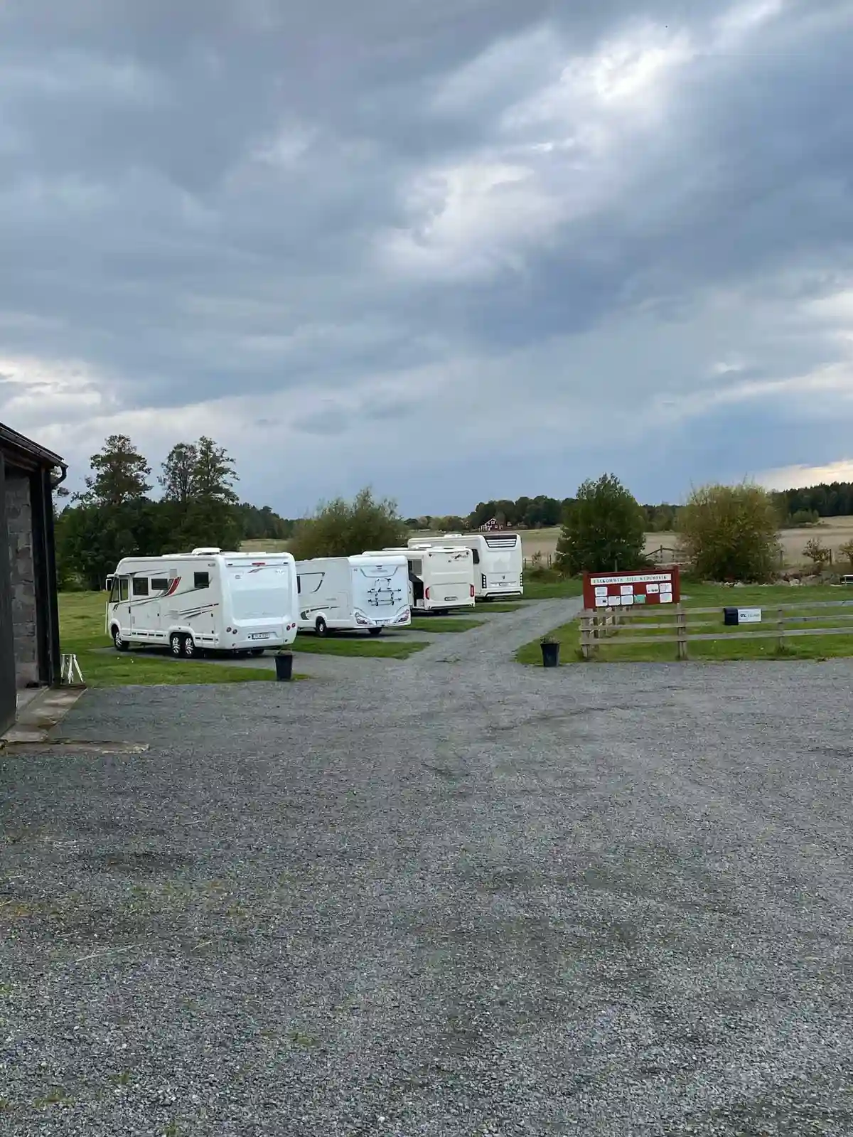 En ställplats för husbilar och husvagnar under en molnig himmel, med flera parkerade fordon på en grusad parkeringsplats.