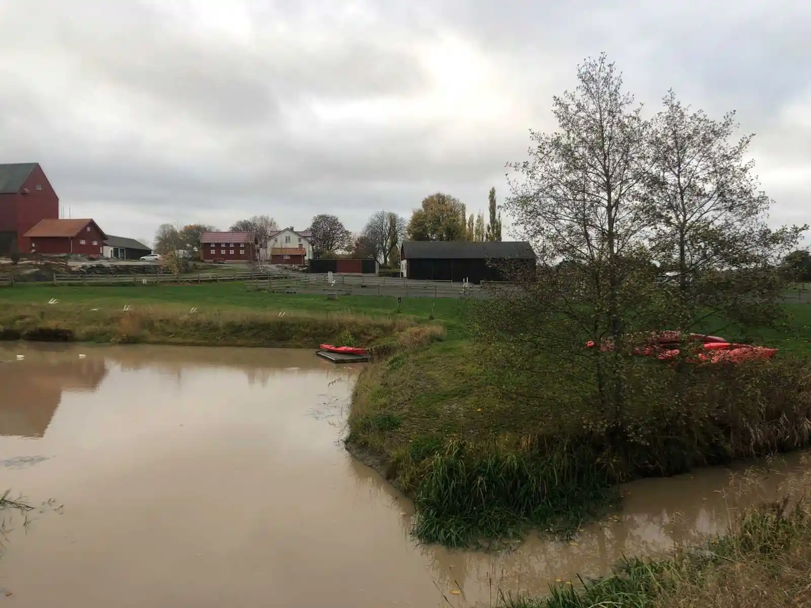 En naturskön ställplats vid Kedumsvik med utsikt över ett vattendrag omgivet av grönska. I bakgrunden syns ett hus vid kanten av det lugna vattnet.