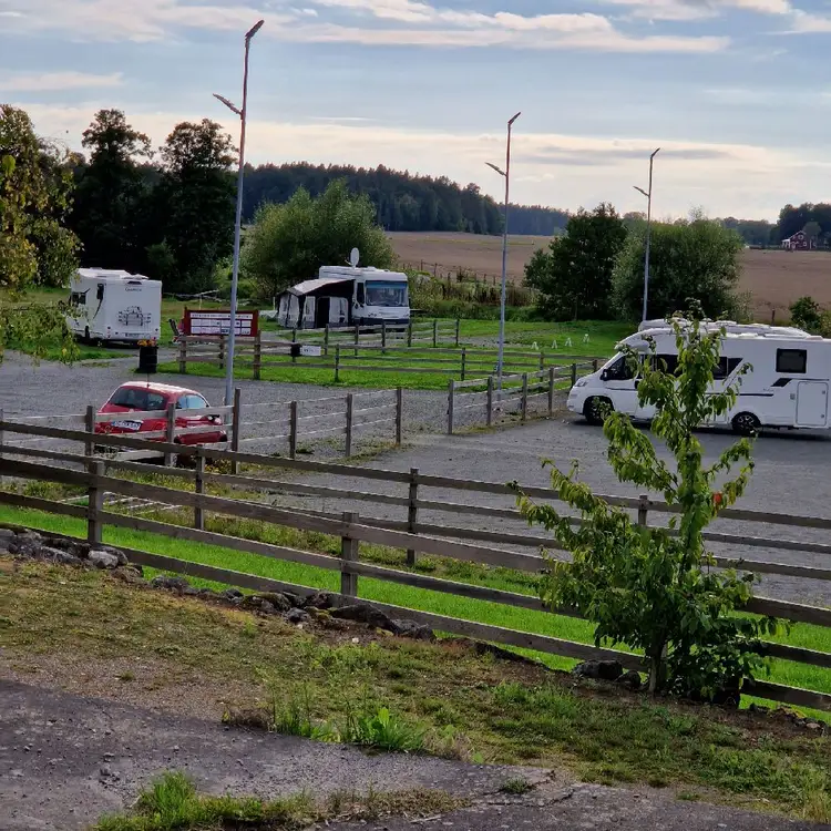 En bil parkerad vid en ställplats i Kedumsvik, omgiven av ett enkelt staket. En familjebil och en lyxig SUV står sida vid sida.