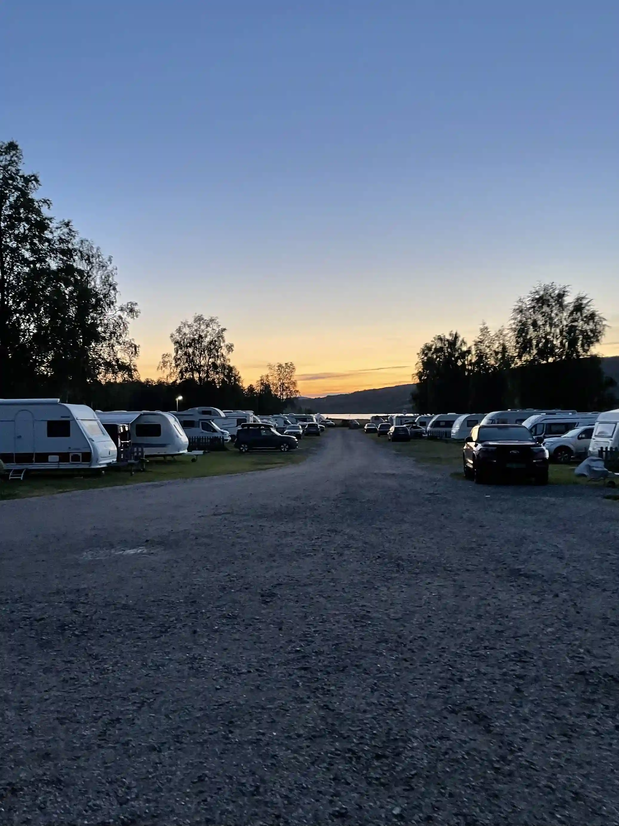 En bil parkerad på campingplatsen i skymningen vid Överhörnäs camping, med ett mjukt ljus som omger campingområdet i bakgrunden.